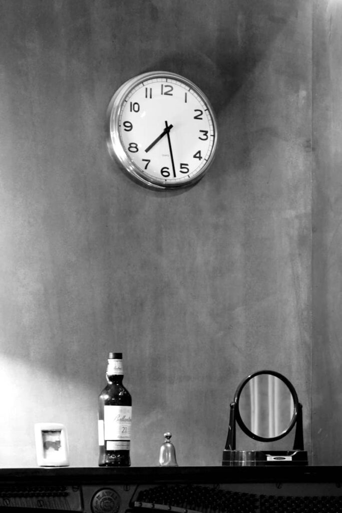 A clock, bottle, and mirror sit on a dark shelf.