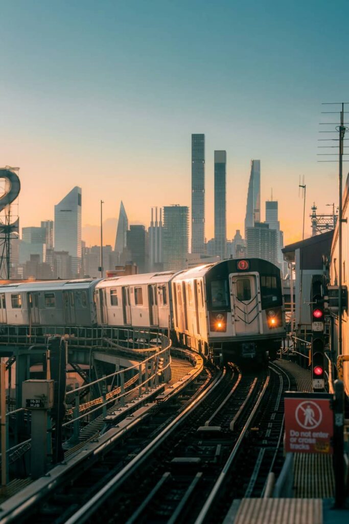 A 7 train on elevated tracks with the New York City skyline at golden hour